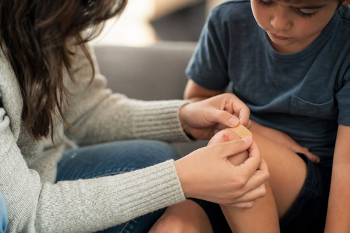 Parent gently applying an Osseus adhesive bandage to a child's scraped knee